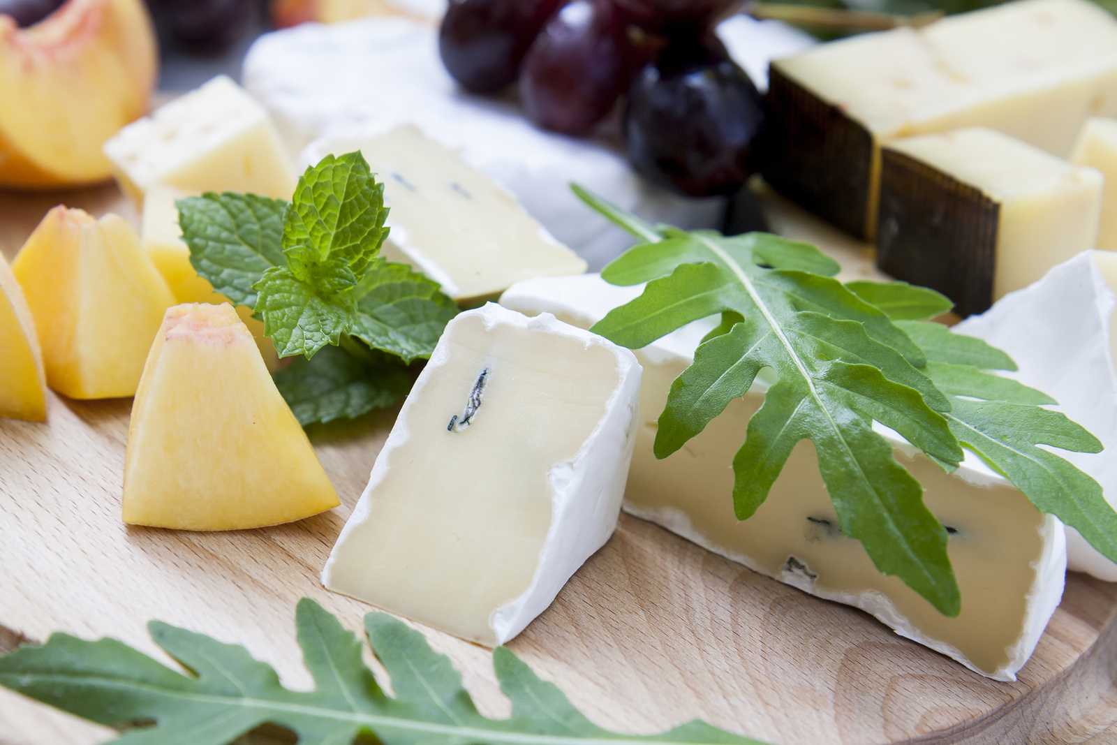 Different Delicious Cheeses And Fruits On Wooden Round Board